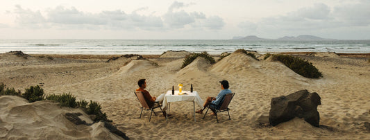 Two people on a beach with an outdoor lamp on a table